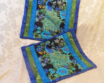 May include: Two blue and green quilted table runners with a peacock design on a black background. The runners have a green, blue, and white border.