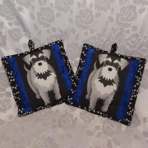 May include: Two black and blue pot holders with a white and gray miniature schnauzer dog design. The pot holders have a black and white polka dot trim.