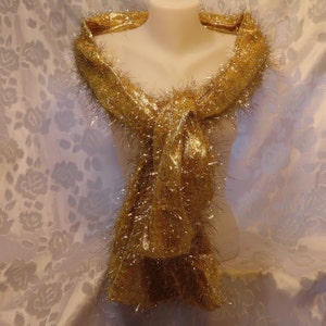 May include: A gold metallic scarf with a fuzzy texture. The scarf is draped over a mannequin's neck.