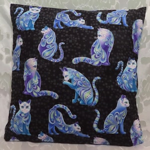 May include: A black pillow with a repeating pattern of blue and purple cats with paisley designs. The cats are in various poses, including sitting, lying down, and standing.