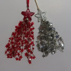 May include: Two star-shaped ornaments with beaded tassels. One ornament is red and the other is clear.