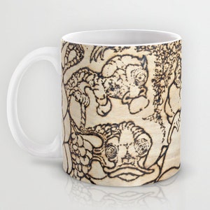 Könnte beinhalten: Weiße Keramiktasse mit einem schwarz-weißen Design aus stilisierten Kreaturen mit großen Augen. Das Design erinnert an Holzbrand.