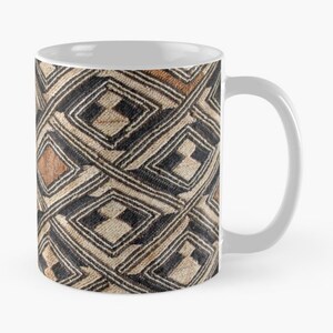 Op de afbeelding: Een witte keramische mok met een bruin en zwart geometrisch patroon. Het patroon bestaat uit herhalende ruiten en lijnen.