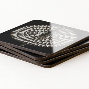 May include: A set of four black square coasters with a white and gray geometric design of a stylized face. The coasters are stacked on top of each other.