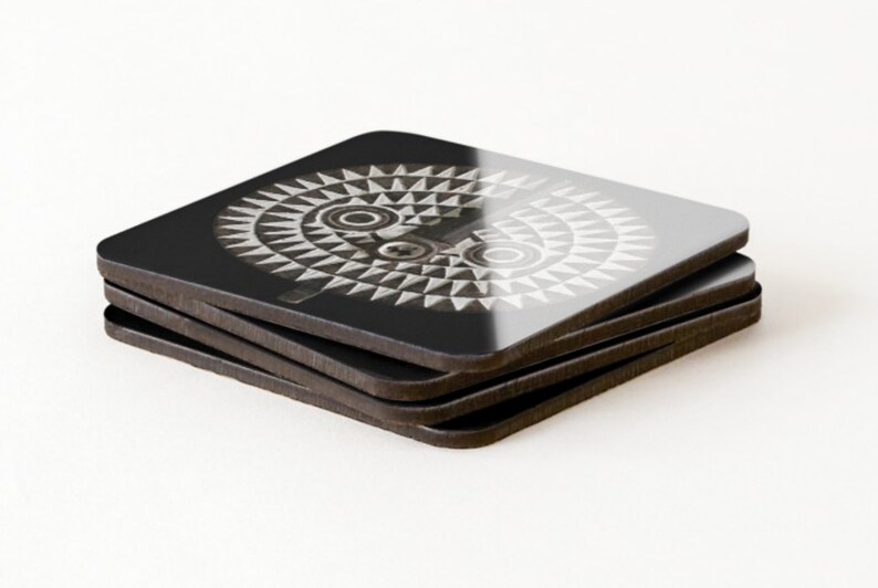 May include: A set of four black square coasters with a white and gray geometric design of a stylized face. The coasters are stacked on top of each other.