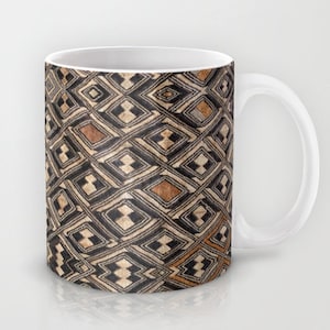 May include: White ceramic coffee mug with a black and brown geometric pattern. The pattern is made up of repeating diamonds and squares.