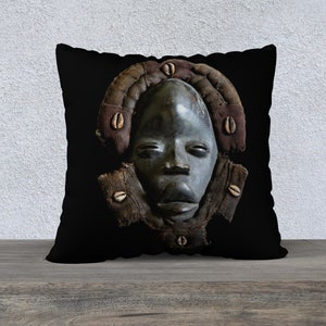 May include: Black and white throw pillow with a dark wooden mask with a human face. The mask is surrounded by a brown and white patterned frame.