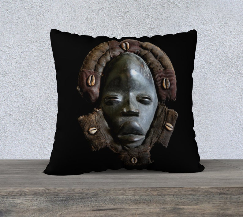 May include: Black and white throw pillow with a dark wooden mask with a human face. The mask is surrounded by a brown and white patterned frame.