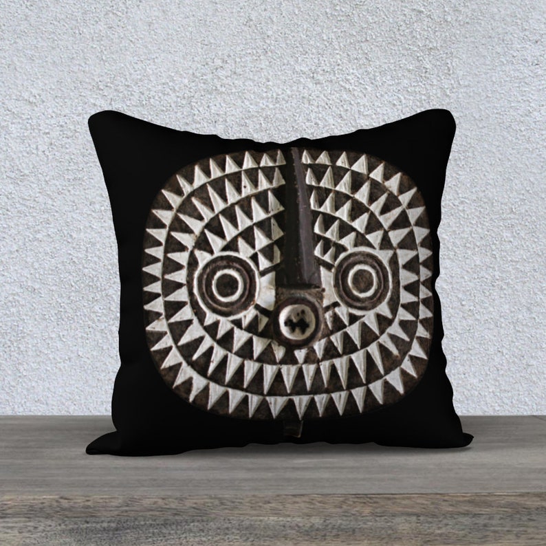 May include: Black and white throw pillow with a geometric design of a stylized face. The pillow has a black background and a white face with a circular pattern.
