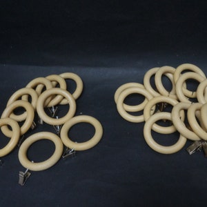 May include: A set of 20 beige wooden curtain rings with silver clips. The rings are arranged in two groups, with one group slightly overlapping the other.