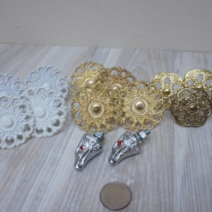 Op de afbeelding: Assortiment van decoratieve ladegrepen in witte en gouden afwerking. De grepen hebben ingewikkelde bloemmotieven. Twee zilveren grepen met rode accenten zijn ook inbegrepen.