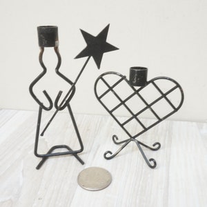 May include: Two black metal candle holders. One is shaped like a person holding a star and the other is shaped like a heart.