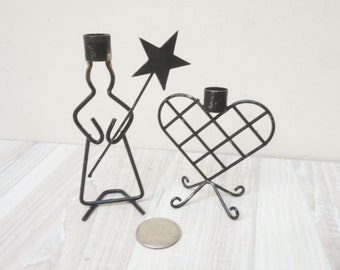 May include: Two black metal candle holders. One is shaped like a person holding a star and the other is shaped like a heart.