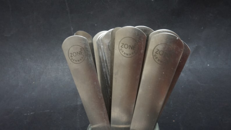 K&ouml;nnte beinhalten: Ein Satz silberfarbener Metallspatel mit dem eingravierten Text "ZONE DENMARK" auf jedem.