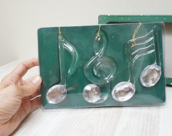 May include: Set of four crystal glass ornaments shaped like musical notes. The ornaments are packaged in a clear plastic box with a green background.