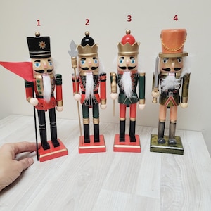 May include: Four wooden nutcracker figurines, each with a different design and color scheme. The nutcrackers are standing on a wooden surface. The nutcrackers are numbered 1 through 4.