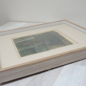 May include: A framed print of a landscape scene with trees and a building in the distance. The print is in shades of gray and brown and is set against a white background.