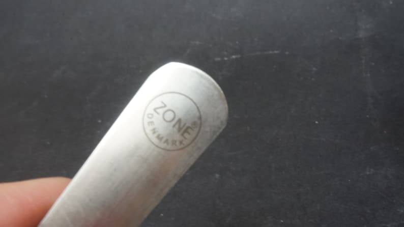 K&ouml;nnte beinhalten: Nahaufnahme eines silbernen Schuhl&ouml;ffels mit dem eingravierten Text "ZONE DENMARK" auf dem Griff.
