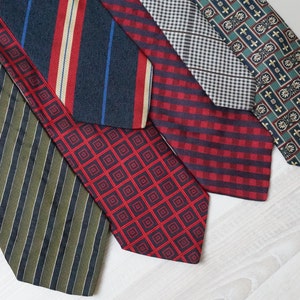 Puede incluir: Cinco corbatas de diferentes patrones en varios colores, incluyendo verde, rojo, azul y blanco. Las corbatas est&aacute;n dispuestas en una fila sobre una superficie de madera blanca.