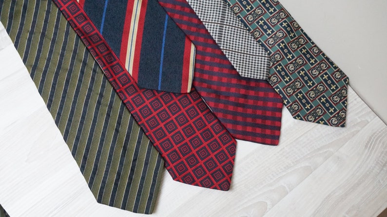 Puede incluir: Cinco corbatas de diferentes patrones en varios colores, incluyendo verde, rojo, azul y blanco. Las corbatas est&aacute;n dispuestas en una fila sobre una superficie de madera blanca.