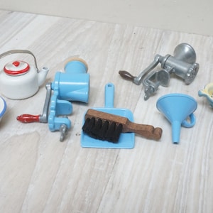 Peut inclure: Un ensemble d'ustensiles de cuisine miniatures, comprenant un bol en émail bleu et blanc, une théière blanche avec un couvercle rouge, un hachoir à viande manuel bleu et blanc, un balai à poussière bleu avec un manche en bois brun et une brosse noire, un entonnoir bleu, une passoire jaune avec une poignée bleue et un hachoir à viande manuel argenté.