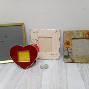 Può includere: Quattro cornici per foto in diversi stili e colori. Una cornice dorata con sfondo grigio, una cornice bianca con un bambino dei cartoni animati, una cornice rossa a forma di cuore con sfondo giallo e una cornice marrone con girasoli.