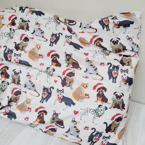 May include: White fabric with a repeating pattern of various dog and cat breeds, each adorned with Santa hats, wreaths, and red bows. The design includes red hearts and gift boxes, creating a festive holiday theme.