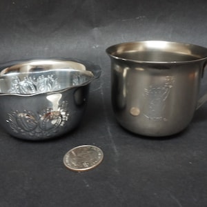 May include: Two silver metal cups, one with a fluted rim and an embossed design, the other with a handle and a plain design.