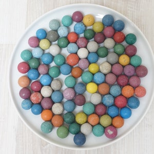 Könnte beinhalten: Ein weißer Teller gefüllt mit bunten Murmeln. Die Murmeln sind in verschiedenen Blautönen, Grüntönen, Rottönen, Gelbtönen und Brauntönen.