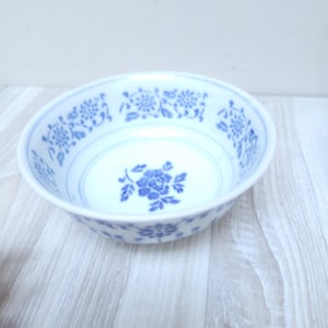 Può includere: Una ciotola in ceramica bianca con un motivo floreale blu. La ciotola ha un design semplice ed elegante con un motivo floreale blu attorno al bordo e un motivo floreale più grande al centro.