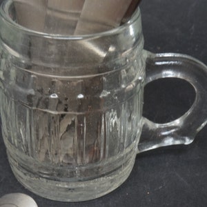K&ouml;nnte beinhalten: Eine klare Glas-Tasse in Form eines Fasses mit einem Henkel. Die Tasse hat eine strukturierte Oberfl&auml;che und ist leer.