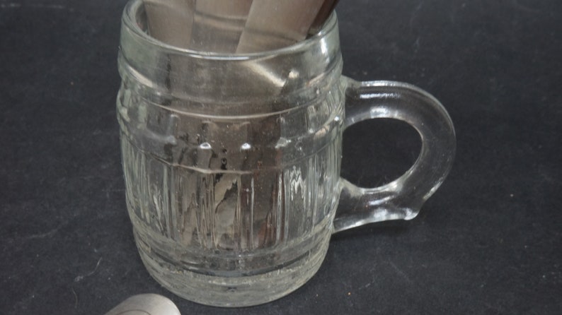 K&ouml;nnte beinhalten: Eine klare Glas-Tasse in Form eines Fasses mit einem Henkel. Die Tasse hat eine strukturierte Oberfl&auml;che und ist leer.