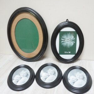 May include: Five oval picture frames, four are black with a raised edge and one is black with a gold inner edge. Three of the black frames have black and white photos of children in them. One of the black frames has a green background with the word "puls" and the text "13 x 18" printed on it. The other frame has a green background.
