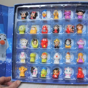 May include: A blue box with a clear plastic insert containing 36 small plastic figurines of Disney characters. The box has a blue background with white stars and the characters are arranged in rows.