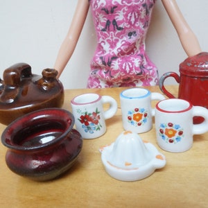 May include: A set of miniature kitchenware, including a brown teapot, a red pot, a red bowl, a white citrus juicer, and four white mugs with floral designs.
