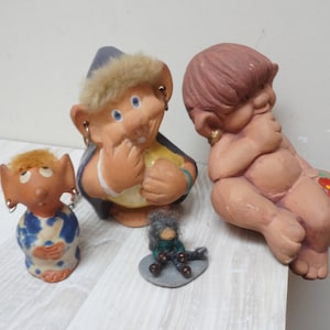 May include: A selection of ceramic figurines, featuring a troll-like character with a blue hat and fur trim, a small seated figure, and a miniature troll on a stone. The figurines are in various colours and styles.