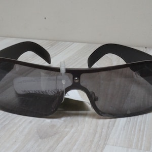 Puede incluir: Gafas de sol negras con montura cuadrada y lentes oscuras. Las gafas de sol están sobre una superficie de madera clara.