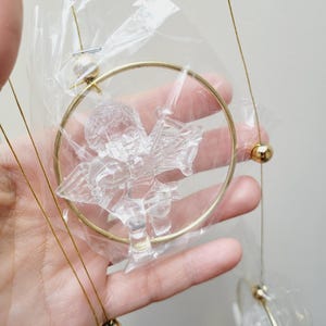 Könnte beinhalten: Ein goldfarbener Windspiel mit klaren Glasengeln und Perlen. Die Engel sind in einem Kreis aufgehängt und die Perlen sind an den Schnüren befestigt.