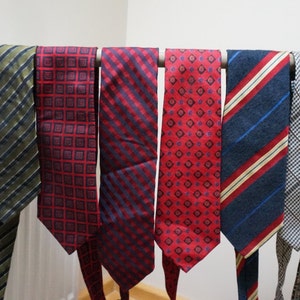 Puede incluir: Ocho corbatas de diferentes patrones colgando de una barra de madera. Las corbatas son de varios colores, incluyendo rojo, azul, verde y negro.