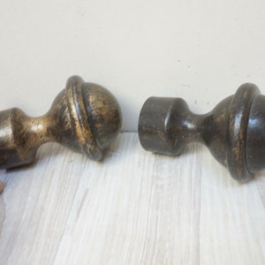 May include: Two wooden finials with a dark brown and gold finish. The finials have a round top and a cylindrical base.