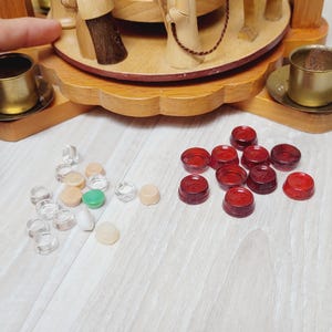 May include: A wooden nativity scene with carved figures and a rotating base. The scene includes figures of the holy family, animals, and other characters. Scattered around are small, red, clear, and opaque game pieces.