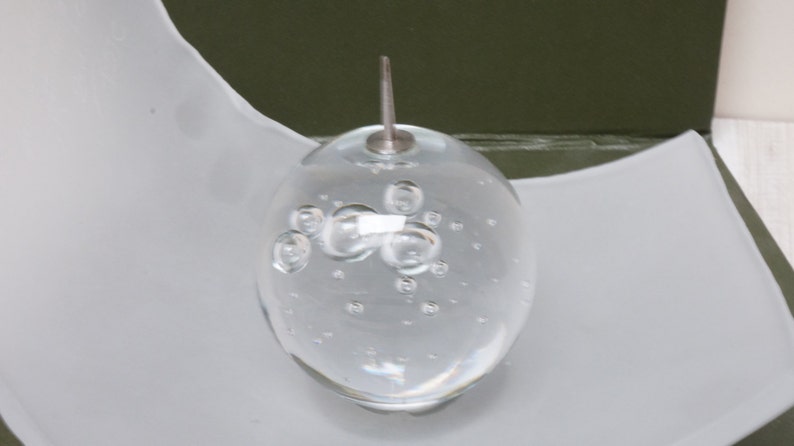 May include: A clear glass sphere with a silver top and many small air bubbles inside. The sphere is sitting on a white surface.