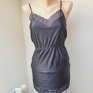Peut inclure: Une robe de dessous noire avec des bordures en dentelle au niveau de l'encolure et de l'ourlet. La robe est sans manches et a un corsage ajusté.