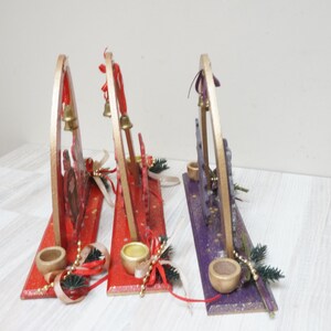 K&ouml;nnte beinhalten: Drei h&ouml;lzerne Weihnachts-Kerzenhalter mit goldenen Akzenten. Die Halter sind mit rotem, violettem und goldenem Glitzer verziert. Jeder Halter hat eine kleine Glocke und einen Kerzenhalter.