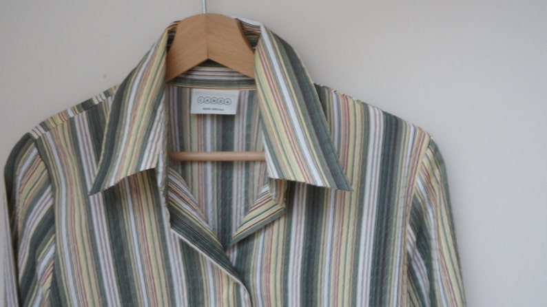 Puede incluir: Una camisa de manga larga a rayas con cuello. La camisa es verde, amarilla, blanca y roja. La camisa tiene una etiqueta que dice "DOCOO".