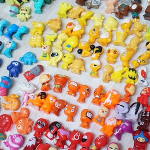 May include: A large collection of colourful plastic figurines. The figurines are arranged in rows by colour, starting with blue, then yellow, orange, and red. The figurines are all different shapes and sizes, and some have unique designs.