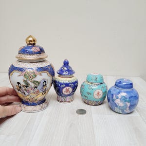 Op de afbeelding: Vier decoratieve porseleinen potten met blauwe en witte bloemenmotieven. De grootste pot heeft een gouden deksel en toont een scène met mensen in traditionele kleding. De kleinere potten hebben Chinese karakters.