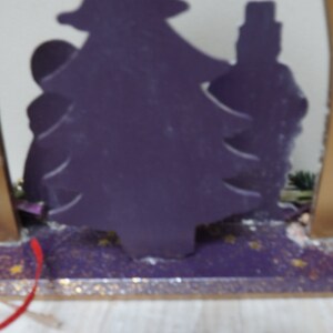 K&ouml;nnte beinhalten: Eine violette Holz-Weihnachtsbaum-Silhouette mit goldenen Kerzenhaltern auf beiden Seiten. Der Baum ist mit goldenem Glitzer verziert und die Basis ist violett mit goldenem Glitzer.