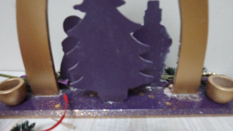 K&ouml;nnte beinhalten: Eine violette Holz-Weihnachtsbaum-Silhouette mit goldenen Kerzenhaltern auf beiden Seiten. Der Baum ist mit goldenem Glitzer verziert und die Basis ist violett mit goldenem Glitzer.