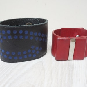 May include: Two leather bracelets. One is black with blue dots and the other is red with a silver buckle.